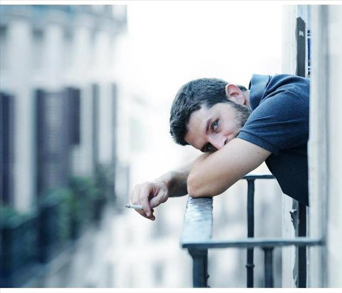 Lonely young man smoking outside at house balcony 
